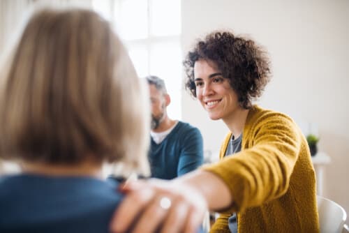 Women in group therapy session lending support to recovering addict