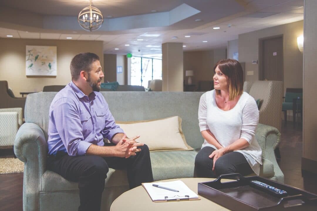 Two people sitting on a couch facing eachother talking about addiction treatment