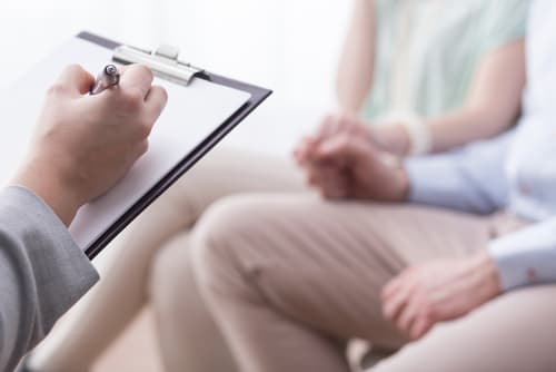 couple sitting on couch with therapist across the way holding clipboard