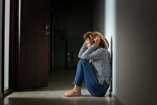 woman sitting on floor against wall holding head in hands